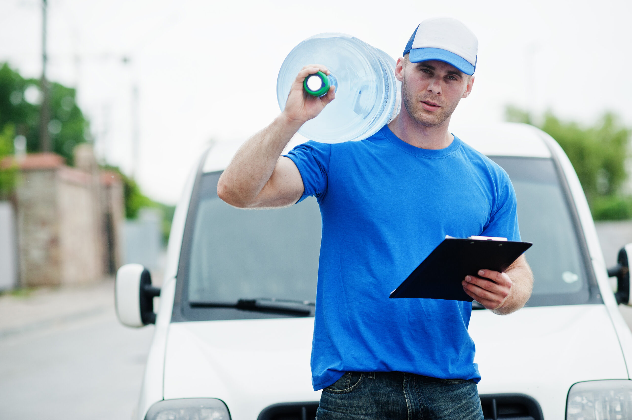 Delivery man with clipboard in front cargo van delivering bottles of water.